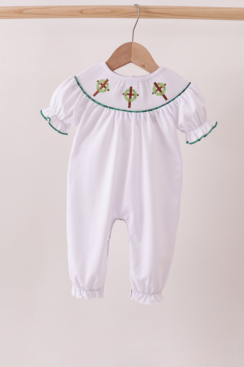 White baby romper with embroidered details on a wooden hanger against a beige background